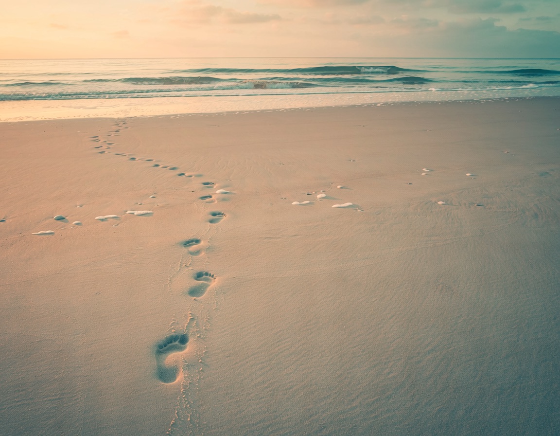 Footprints leading toward the ocean at sunrise